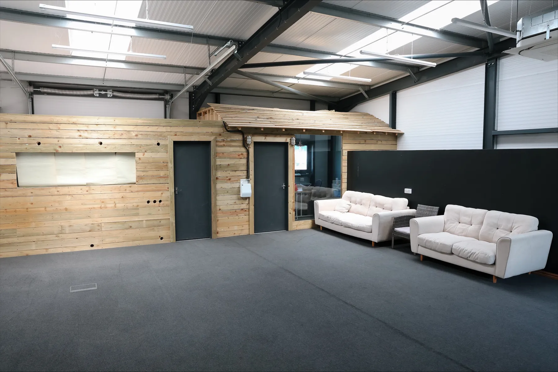 The upstairs event space: a timber-clad wall with two doors, two cream sofas and a grey carpet under a high roof