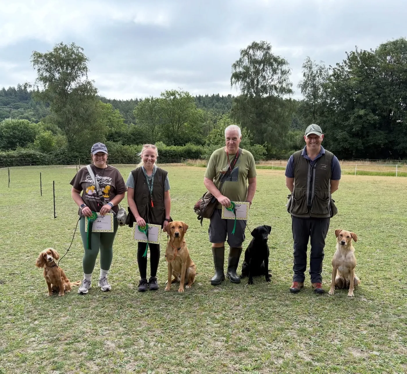 Four handlers and their dogs lined up on a field with their gun-dog course certificates