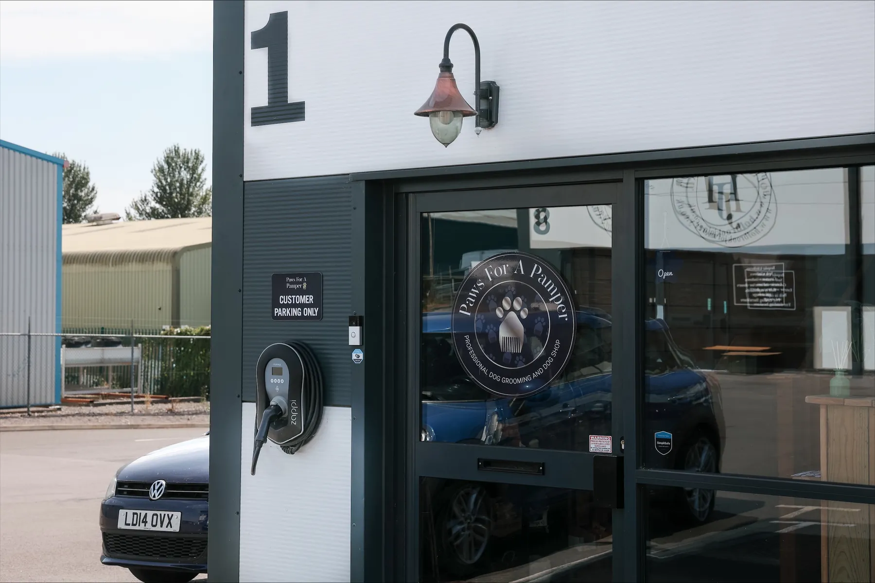 The front door of Unit W1 with the round Paws For A Pamper sign in the glass and a customer parking sign beside it