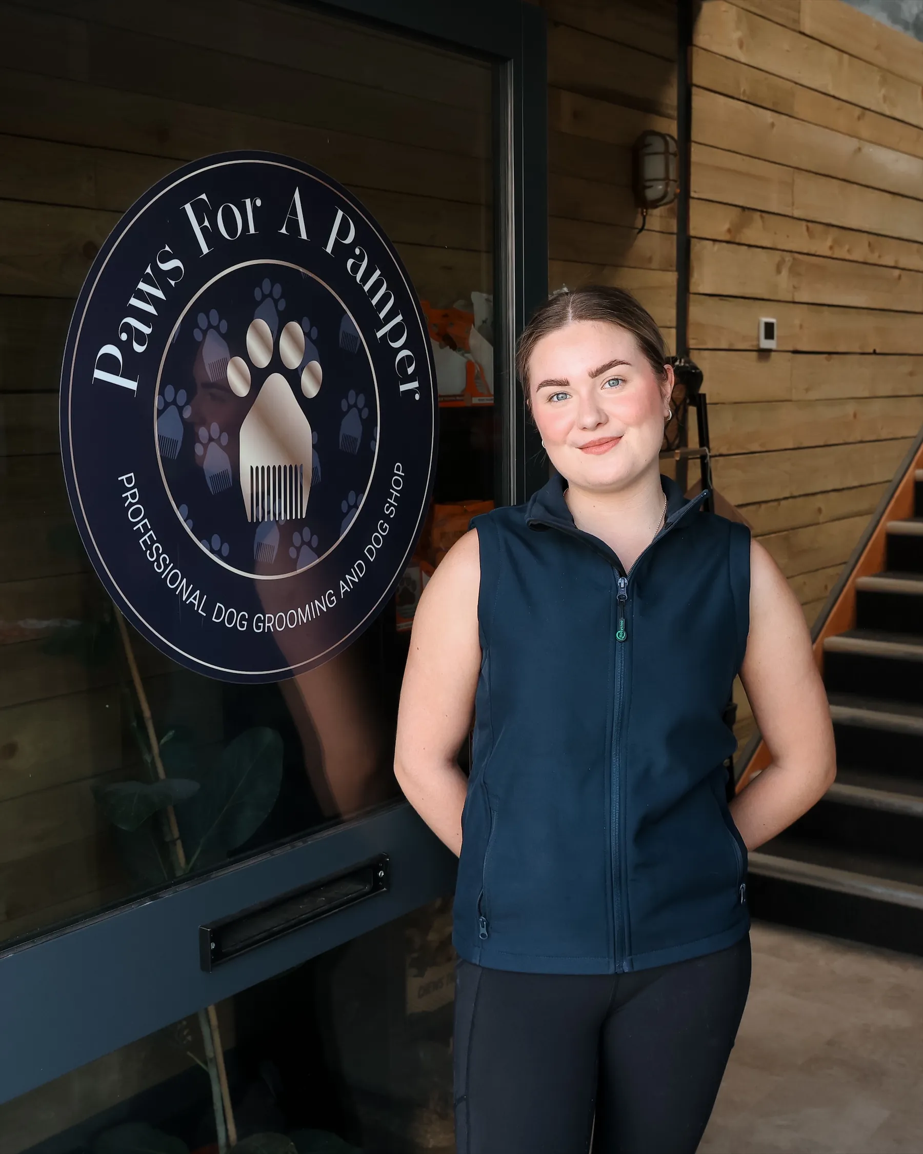 Meg, apprentice dog groomer, standing by the round Paws For A Pamper sign